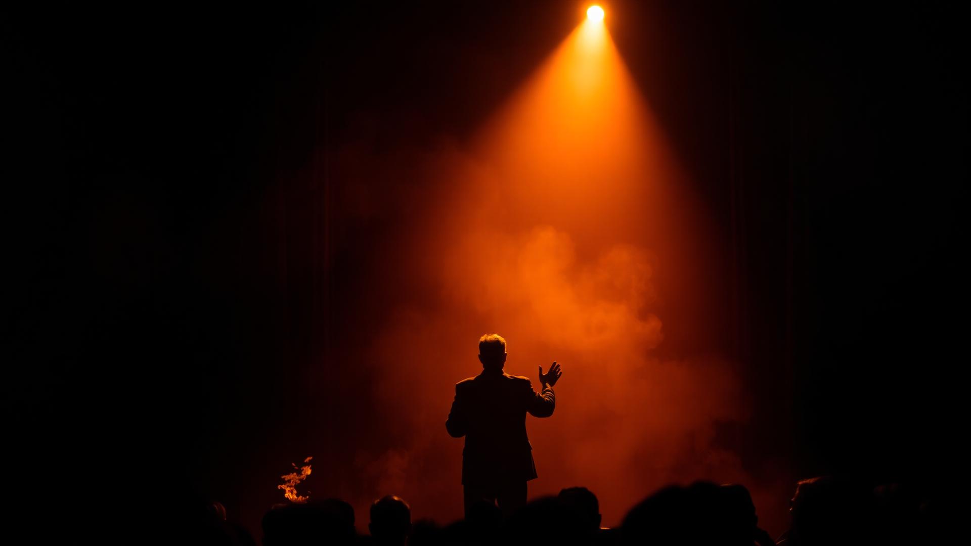 A preacher under a spotlight on a smoky stage